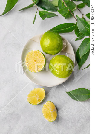 Fresh juicy limes in a plate on a light background with leaves and citrus pieces. 119858374