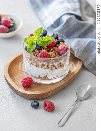 Natural yogurt with granola, raspberries and blueberries in a glass on a wooden board Natural yogurt with granola, raspberries and blueberries in a glass on a wooden board 119858376