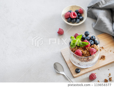 Greek yogurt with granola, raspberries and blueberries in a glass on a wooden board Greek yogurt with granola, raspberries and blueberries in a glass on a wooden board 119858377