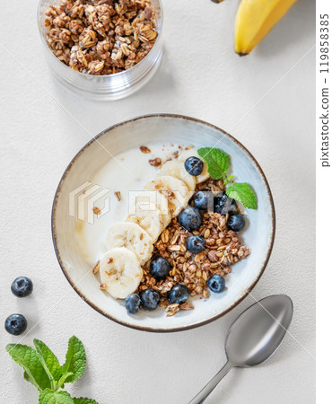 Flat lay of granola with yogurt, banana and blueberries in a bowl on a light background Flat lay of granola with yogurt, banana and blueberries in a bowl on a light background 119858385