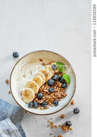 Natural yogurt with granola or muesli, banana and blueberries in a bowl on a white background 119858389