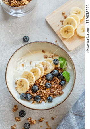 Natural yogurt with granola or muesli, banana and blueberries in a bowl on a white background 119858391