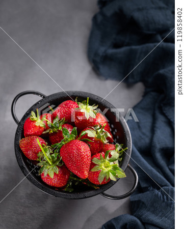 Ripe strawberries in a black bowl on a dark background with a napkin and shadows. Ripe strawberries in a black bowl on a dark background with a napkin and shadows. 119858402