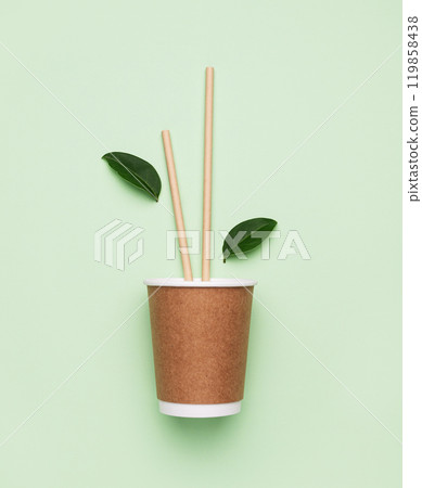 Brown paper coffee cup on green background with bamboo straws and leaves. Brown paper coffee cup on green background with bamboo straws and leaves. 119858438