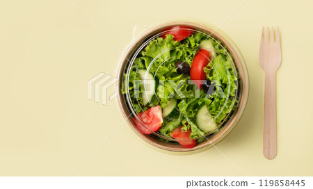 Fresh salad in eco-friendly container with wooden fork on yellow background. 119858445