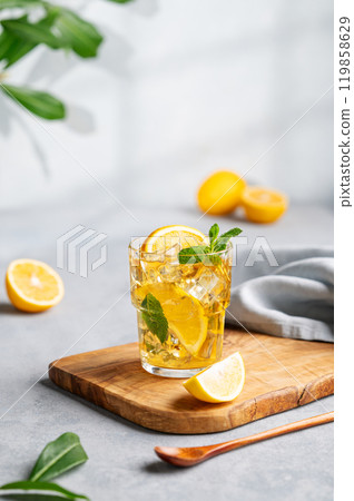 Iced tea with lemon, mint and ice in a glass on a wooden board on a light background Iced tea with lemon, mint and ice in a glass on a wooden board on a light background 119858629