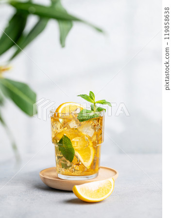 Iced tea with lemon, mint in a glass on light background with shadow and branch. 119858638