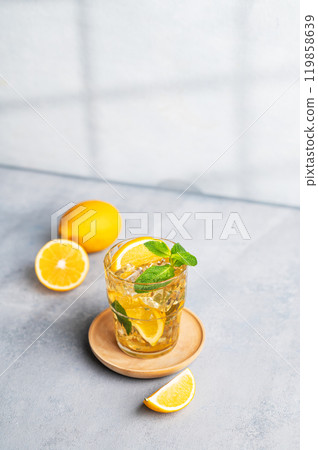 Iced tea with lemon, mint in a glass on light background with shadow and citrus fruits. 119858639