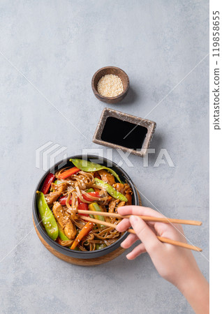 Stir-fry with soba noodles, meat and vegetables in black plate on a light background Stir-fry with soba noodles, meat and vegetables in black plate on a light background 119858655