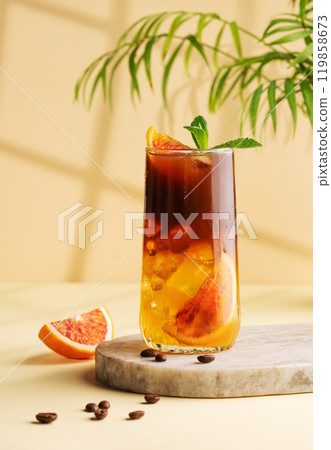 Americano coffee with orange juice (bumble) in a tall glass with ice and mint on a yellow background Americano coffee with orange juice (bumble) in a tall glass with ice and mint on a yellow background 119858673