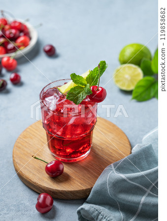 Cherry-lime mojito cocktail with mint, lime and ice on a wooden board on a blue background 119858682