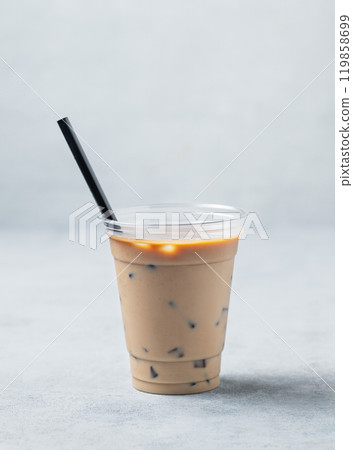Iced coffee in a recyclable plastic glass with milk and ice on a light background. Iced coffee in a recyclable plastic glass with milk and ice on a light background. 119858699