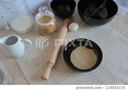Baking ingredients for baking sweet buns, yeast in black bowl dishes with rolling pin on a table Baking ingredients for baking sweet buns, yeast in black bowl dishes with rolling pin on a table 119858729