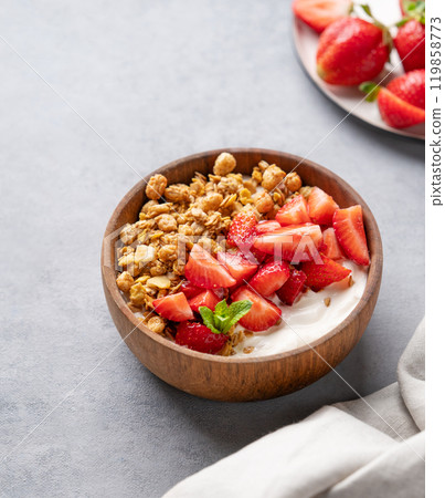 Natural yogurt with granola and strawberries in a wooden bowl on a blue background Natural yogurt with granola and strawberries in a wooden bowl on a blue background 119858773