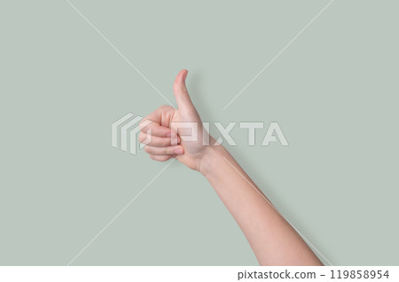 Hand shows thumb up on a light green background. Sign language concept ok. Hand shows thumb up on a light green background. Sign language concept ok. 119858954