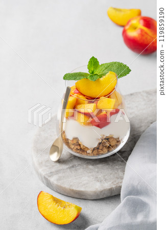 Greek yogurt parfait with peach and muesli in a glass on a marble board on a light background  119859190