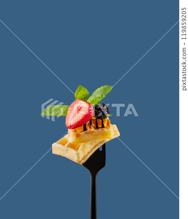 Wafer pieces with fresh strawberries, blackberries, mint leaves  on a black fork on  blue background 119859205
