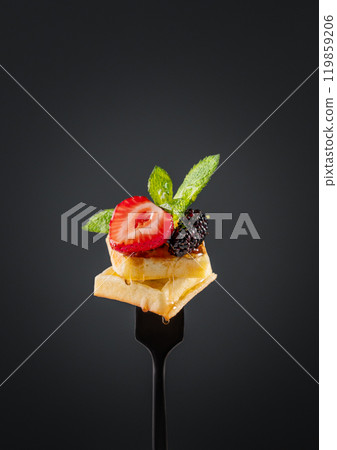 Wafer pieces with fresh strawberries, blackberries, mint leaves and dripping honey on a black fork 119859206