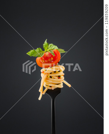 Spaghetti on a black fork with a piece of tomato, sauce and basil on a dark background.  119859209