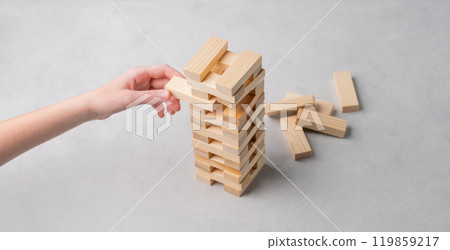 A hand pulls out a piece from a wooden tower game on a light background. 119859217