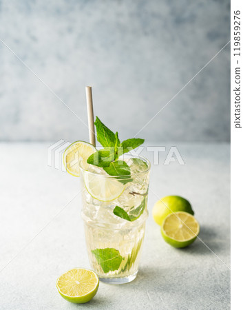 Mojito cocktail in a tall glass with lime, mint and ice on a light textured background. Mojito cocktail in a tall glass with lime, mint and ice on a light textured background. 119859276