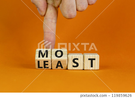 Most or least symbol. Businessman turns beautiful wooden cubes and changes the word Least to Most. Beautiful orange table orange background. Copy space. Business and most or least concept. 119859626