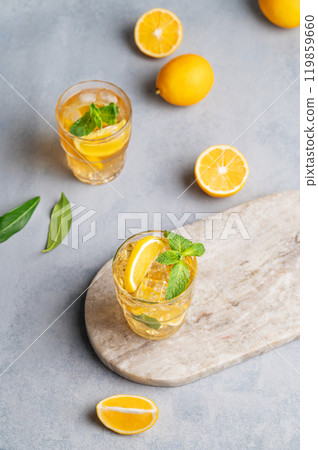 Iced tea with lemon, mint in a glass on a marble board on a light background with citrus fruits. Iced tea with lemon, mint in a glass on a marble board on a light background with citrus fruits. 119859660