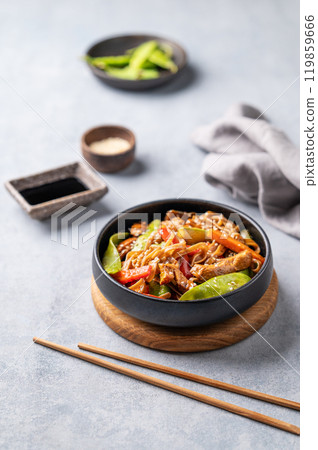 Stir-fry with soba noodles, meat and vegetables on a light background with chopsticks, soy sauce Stir-fry with soba noodles, meat and vegetables on a light background with chopsticks, soy sauce 119859666