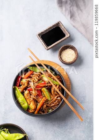 Stir-fry with soba noodles, meat and vegetables on a light background with chopsticks, soy sauce Stir-fry with soba noodles, meat and vegetables on a light background with chopsticks, soy sauce 119859668