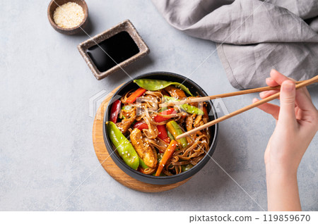 Stir-fry with soba noodles, meat and vegetables in black plate on a light background Stir-fry with soba noodles, meat and vegetables in black plate on a light background 119859670