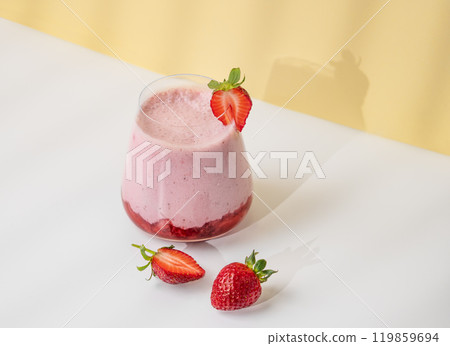 A strawberry milkshake or smoothie in a glass with strawberries on a yellow background 119859694