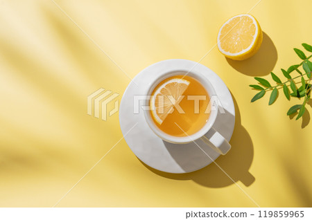 Herbal tea with lemon in a white cup on a yellow background with shadows. 119859965