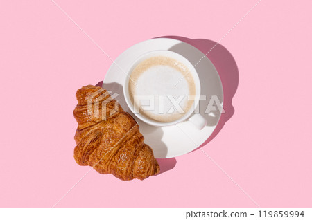 Flat lay of coffee cup and fresh croissant on a white plate on a pink background. 119859994
