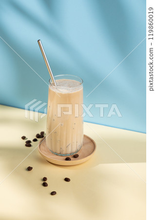 Iced coffee in a tall glass with a milk jug pouring milk on a blue and yellow background  119860019