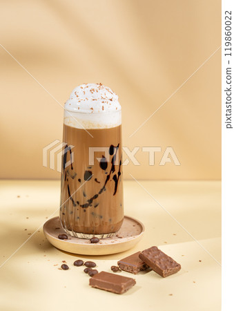 Cold chocolate coffee drink or milkshake with whipped cream in a tall glass on a yellow background 119860022