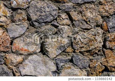 Textured stone wall composed of various sized rocks, showcasing natural colors and patterns under bright daylight 119860142