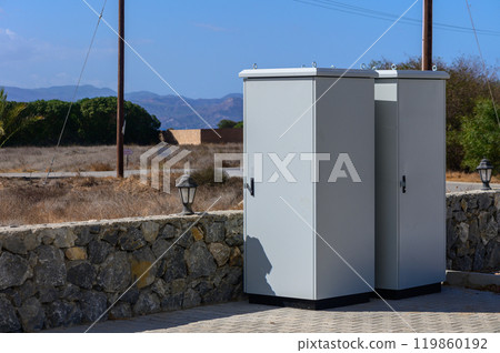 Two utility boxes stand against a backdrop of dry grass and distant mountains on a sunny day 119860192