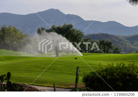 A tranquil early morning on a lush golf course with mist rising from sprinklers amid distant mountains A tranquil early morning on a lush golf course with mist rising from sprinklers amid distant mountains 119860206