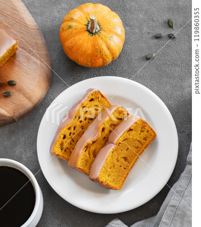 Pumpkin sweet bread or cake with icing on a plate on a dark background with decorative pumpkins 119860355