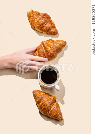 Hand holding fresh croissant on yellow background with shadow and cup of espresso coffee. 119860371