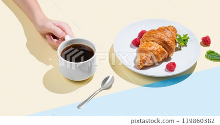 Hand holding a cup of espresso coffee on a yellow and blue background with shadow and croissants  119860382