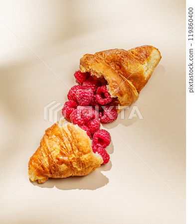 Flat lay of broken croissant with fresh raspberries on yellow background with shadow. 119860400