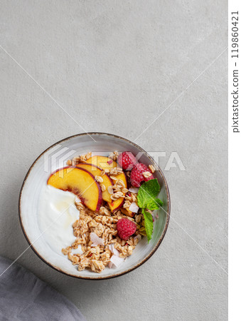 Greek natural yogurt with oat granola or muesli, peach, raspberry and mint in a bowl Greek natural yogurt with oat granola or muesli, peach, raspberry and mint in a bowl 119860421