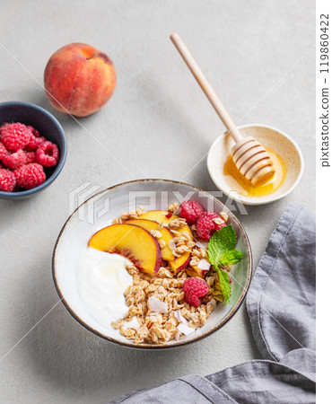 Greek natural yogurt with oat granola or muesli, peach, raspberry and honey in a bowl Greek natural yogurt with oat granola or muesli, peach, raspberry and honey in a bowl 119860422
