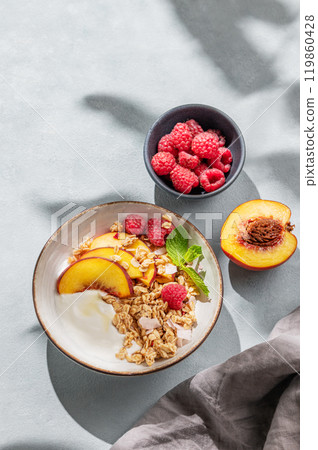 Flat lay of natural yogurt with oat granola, peach and raspberry in a bowl on a light background Flat lay of natural yogurt with oat granola, peach and raspberry in a bowl on a light background 119860428