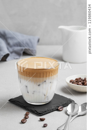 Iced dalgona coffee. Whipped instant coffee in glass with ice on a slate board on a gray background 119860434