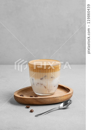 Dalgona coffee. Whipped instant coffee in a glass with ice on a wooden board on a gray background Dalgona coffee. Whipped instant coffee in a glass with ice on a wooden board on a gray background 119860439