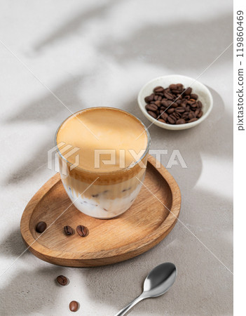 Dalgona coffee. Whipped instant coffee in a glass with ice on a wooden board on a gray background 119860469