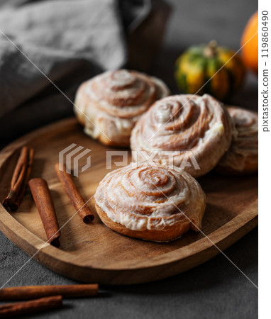 Sweet rolls with cinnamon and icing on a wooden board on a dark background. 119860490