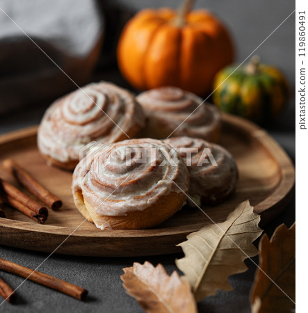 Sweet rolls with cinnamon and icing on a wooden board on a dark background with pumpkin. Sweet rolls with cinnamon and icing on a wooden board on a dark background with pumpkin. 119860491